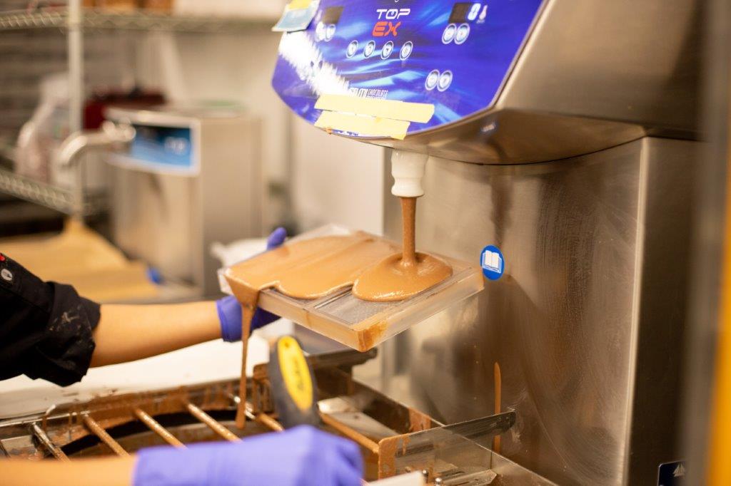 Image of handing using chocolate machine putting chocolate into molds for bonbons