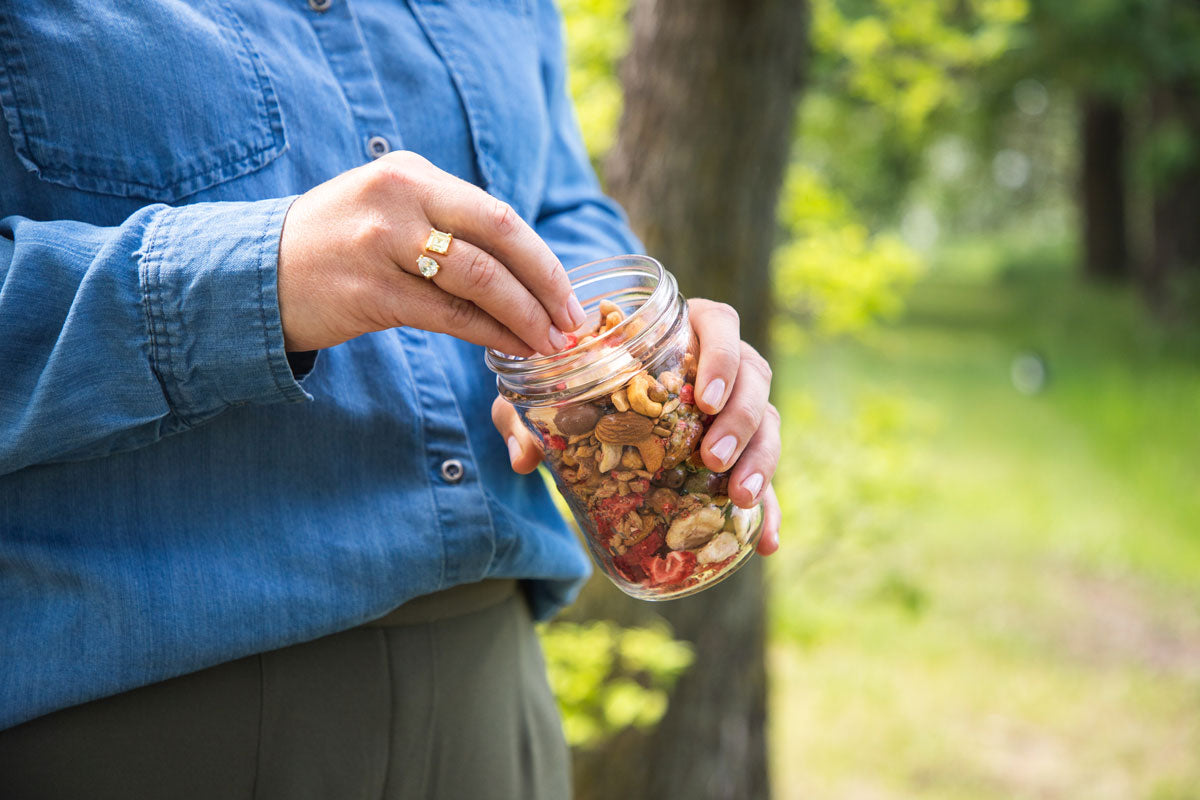 Image of hand picking trail mix out of a mason jar while in the forest
