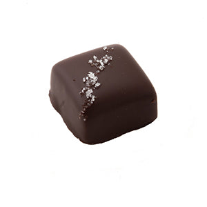 A square shaped caramel, enrobed in dark chocolate and sprinkled with sea salt.